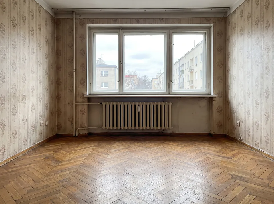 Salon mieszkania do remontu ze starym parkietem i tapetą, sfotografowany w dziennym świetle do ogłoszenia sprzedaży